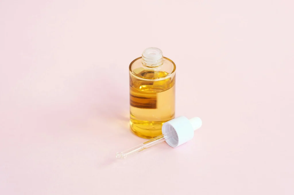 Pembe zemin üzerinde altın renkli serum şişesi ve damlalık